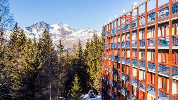 A multi-story hotel with a mountain backdrop, surrounded by trees and snow.