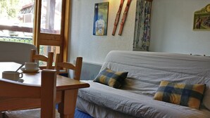 A cozy room with a bed, a table with a cup and saucer, and skis leaning against the wall.
