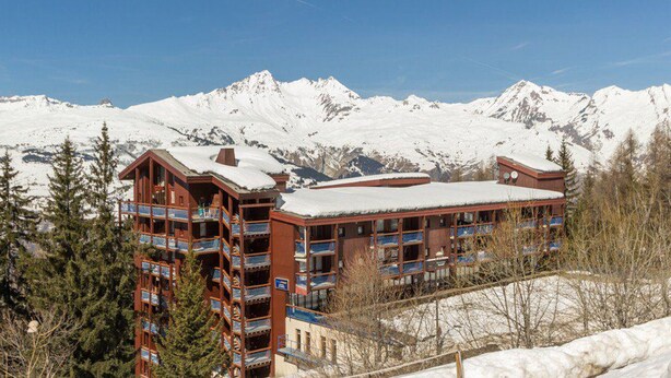 Um hotel com vários andares, varandas e uma montanha coberta de neve ao fundo.