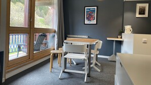 Uma cozinha moderna com mesa e cadeiras de madeira, uma luminária pendente amarela e vista para o exterior através de grandes janelas.
