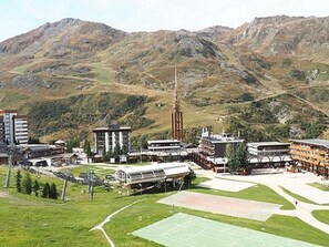 A mountainous landscape with a central building featuring a tall tower, surrounded by smaller buildings and green spaces.