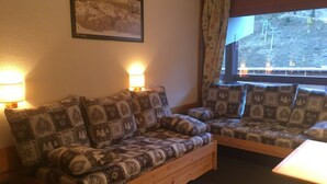 Um quarto aconchegante com um sofá de madeira e uma janela com vista para uma montanha.