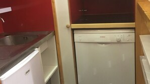 Uma cozinha compacta com máquina de lavar louça Bosch, geladeira branca e micro-ondas sobre a máquina de lavar.