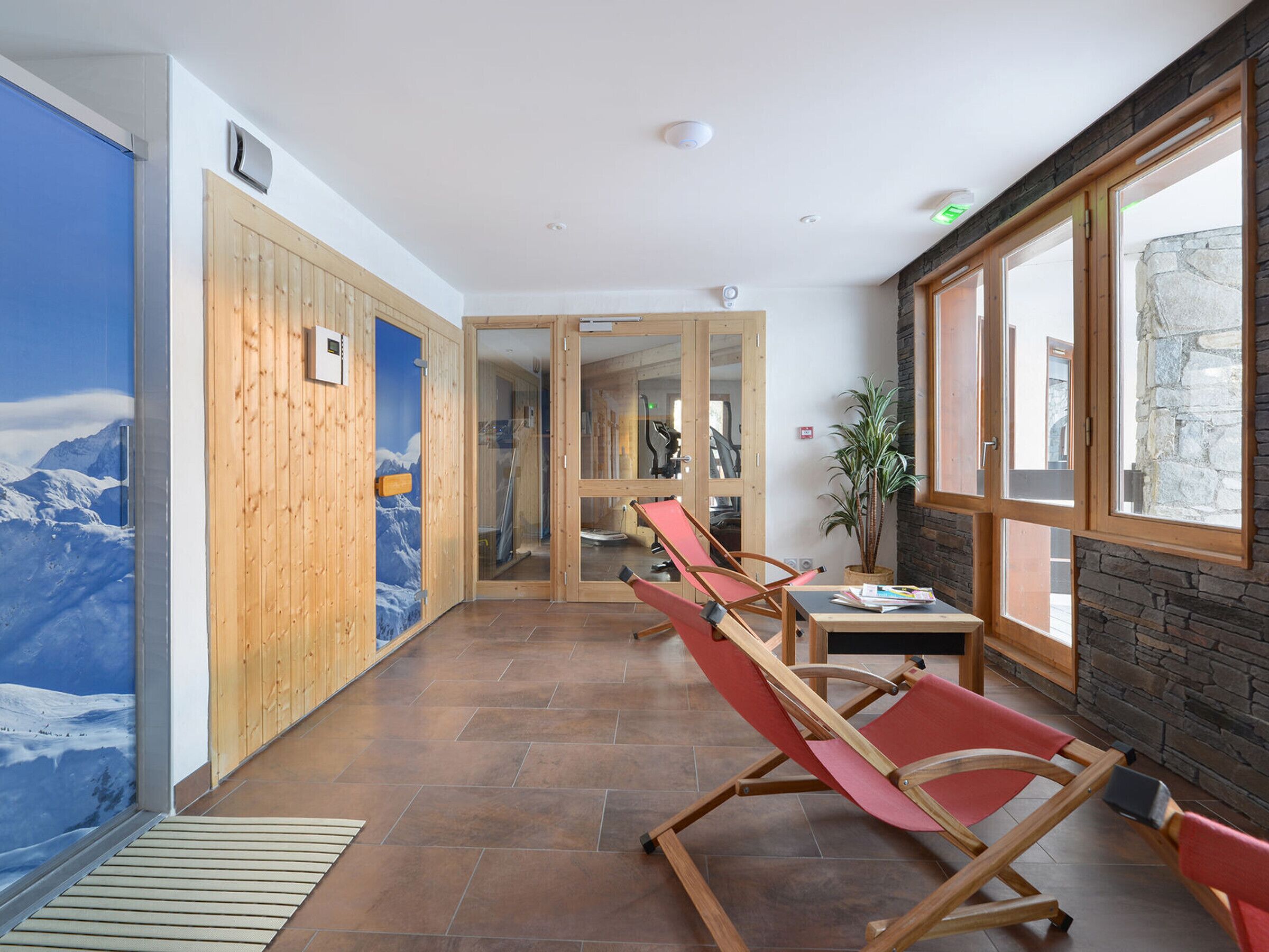 A corridor with wooden walls, a mountain mural, and a red lounge chair.