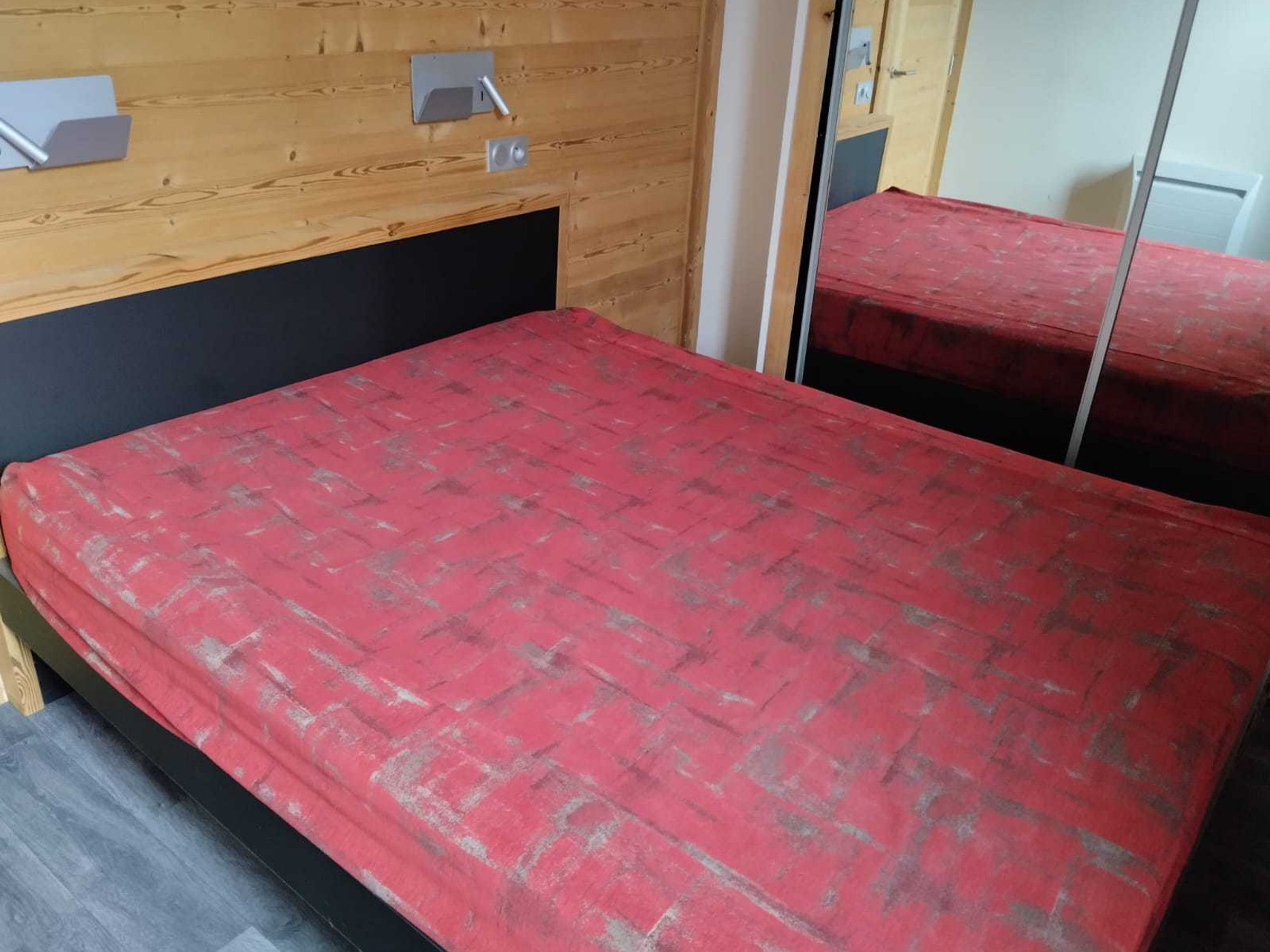 A room with a bed, a wooden headboard, a mirror, and a door.