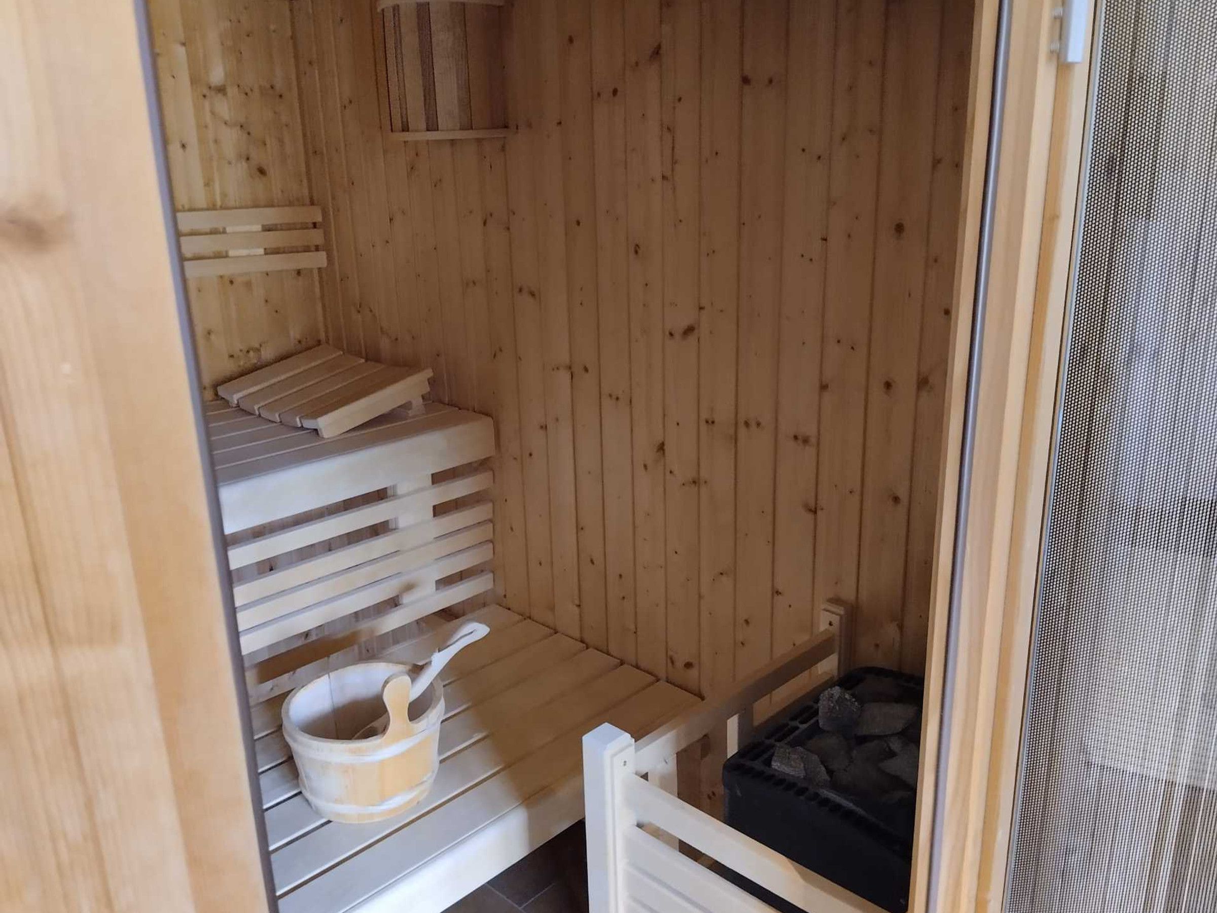 A sauna room with wooden benches and a small wooden bucket.