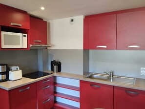 Eine kompakte Küche mit roten Schränken, einer Mikrowelle, einem Toaster und einem Spülbecken.