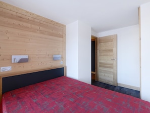 Ein Schlafzimmer mit einem Holzkopfteil, einem mit rotem Teppich bedeckten Bett, einer weißen Wand und einer Holztür.