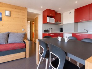 Eine moderne Küche mit roten Schränken, einem Esstisch und einem Holzsofa mit Kissen.
