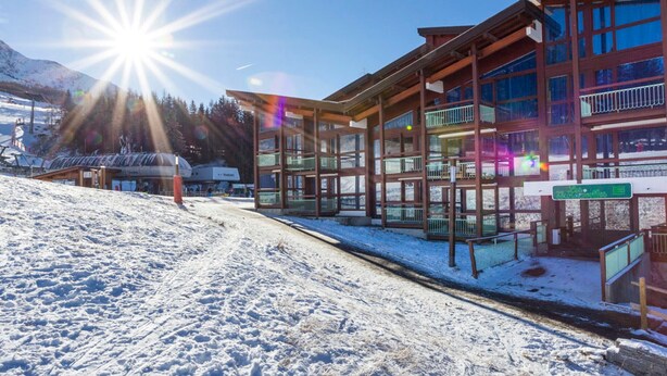 A modern ski resort building with multiple balconies and large windows, surrounded by snow-covered terrain and mountains.
