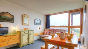 A cozy room with a wooden dresser, a television, a patterned sofa, and a dining table with bowls and cups.