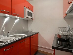 A compact kitchen with red cabinets, a stainless steel sink, a microwave, and a coffee maker.
