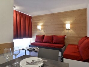 A hotel room with a wooden headboard, two red pillows, a small table with a plate, cutlery, and wine glasses.