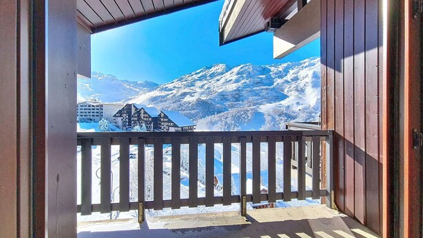 Un balcón con vista a montañas nevadas y un edificio al fondo.