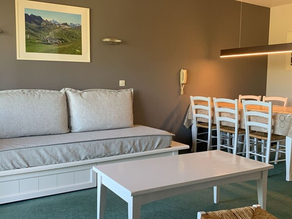 Un soggiorno con divano, un tavolo da pranzo con sedie, un quadro paesaggistico incorniciato e un telefono appeso al muro.