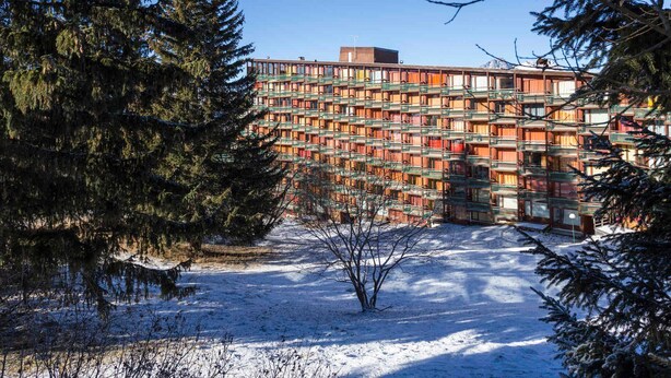 A multi-story building with a unique facade of colorful, stacked windows, surrounded by snow-covered ground and evergreen trees. - Renovated Studio 5 ppl · Ski-in/Ski-out · Balcony · Pets Allowed (Les Arcs 1800)
