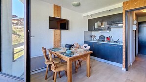 Eine kompakte Küche mit modernen Geräten, ein Essbereich mit Holzmöbeln und ein Blick durch eine Glastür.