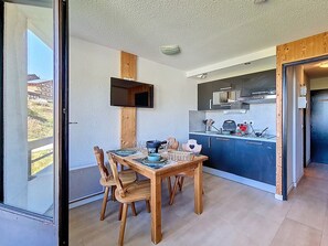 Eine kompakte Küche mit modernen Geräten, ein Essbereich mit Holzmöbeln und ein Blick durch eine Glastür.