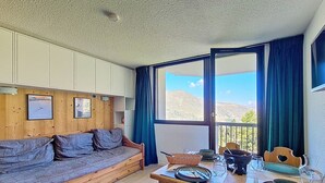Ein gemütliches Zimmer mit einer Holzsofa, einem Esstisch mit Tellern und Gläsern sowie Bergblick durch große Fenster.