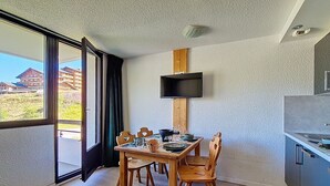 Eine moderne Küche mit Einbauherd, einem Essbereich mit Holztischen und -stühlen sowie einem großen Fenster mit Blick auf umliegende Gebäude.