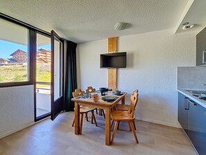 Eine moderne Küche mit Einbauherd, einem Essbereich mit Holztischen und -stühlen sowie einem großen Fenster mit Blick auf umliegende Gebäude.
