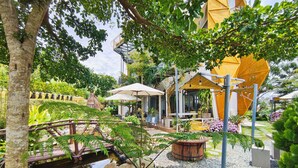 Ein Garten mit Teich, Holzbrücke und Sitzbereich im Freien mit Sonnenschirmen.