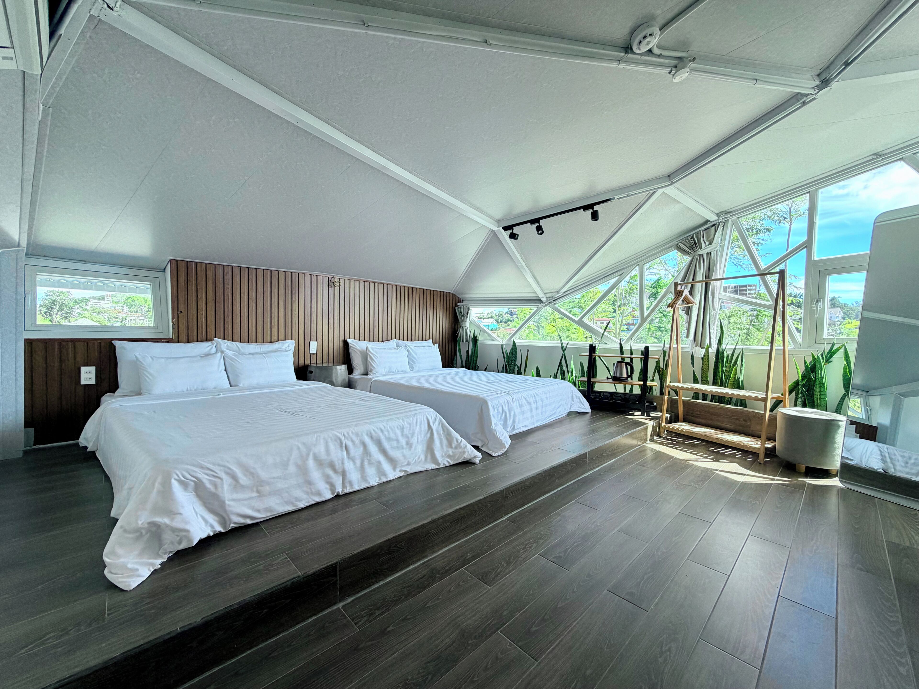 Ein modernes Zimmer mit zwei Betten, einem Holzkopfende, einem großen Fenster und Blick ins Grüne.
