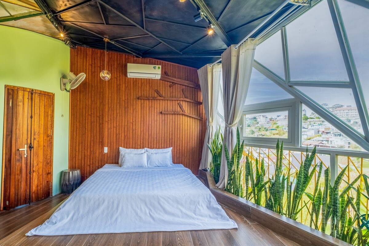 Une chambre dotée d’un grand lit, de murs en bois, d’un appareil de climatisation et offrant une vue sur le paysage urbain grâce à de grandes fenêtres.