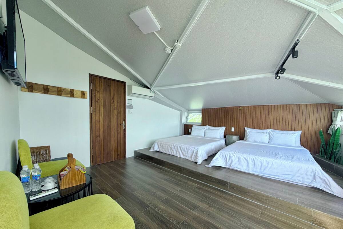 Une chambre avec deux lits, une porte en bois, une petite table avec des bouteilles d’eau et une chaise verte.