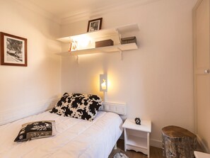 Un dormitorio con cama, mesita de noche, estantería con libros y un cuadro en la pared.