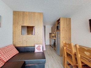 A compact living space with a wooden wall, a sofa, a small table, and a kitchenette.