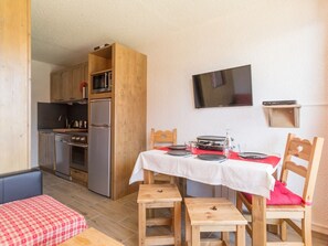 A compact kitchen with modern appliances, a dining area with a table set for two, and a television mounted on the wall.