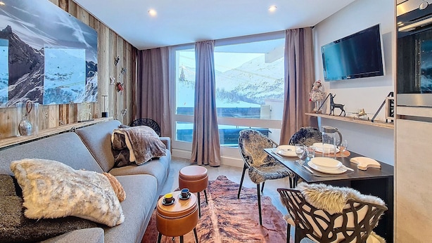 Una sala de estar moderna con sofá, sillas, una mesa de comedor y un ventanal con vistas a un paisaje nevado.