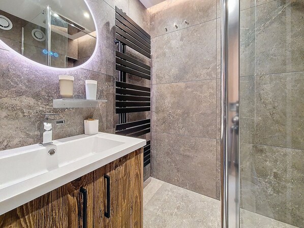 A modern bathroom with a white sink, wooden cabinet, and a glass shower enclosure.