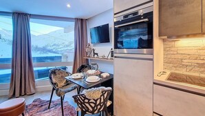 Una cocina moderna con horno empotrado y protector contra salpicaduras de piedra, un área de comedor con mesa y sillas, y un ventanal con cortinas.