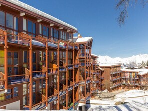 A multi-story hotel with balconies, large windows, and a snowy mountain backdrop.