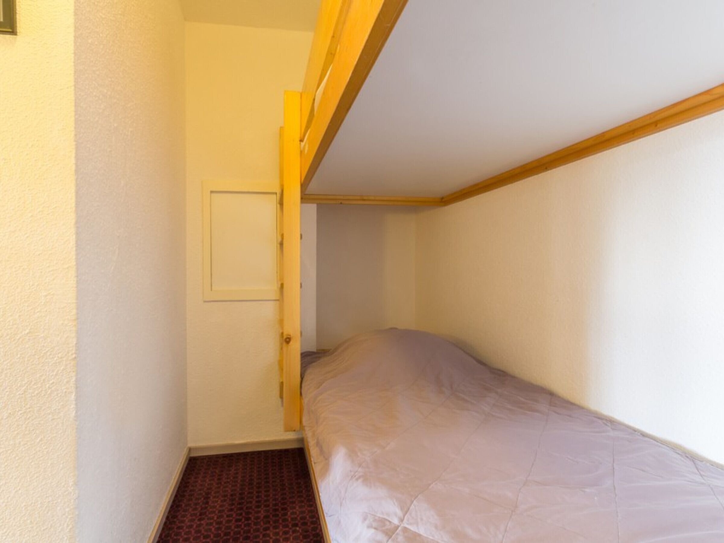 Um quarto pequeno e estreito com uma cama beliche, uma porta e um chão estampado.