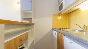 Une cuisine compacte avec des meubles blancs, un four à micro-ondes, un lave-vaisselle et un évier avec un pare-éclaboussures jaune.