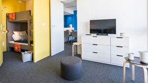 Une chambre d’hôtel moderne équipée d’un lit superposé, d’un téléviseur à écran plat, d’une commode blanche et d’une petite table avec une tasse.