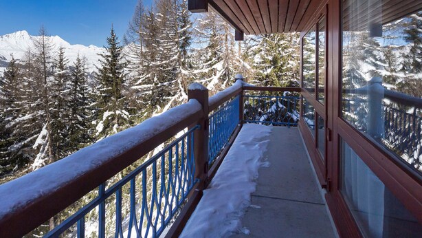 Un balcon offrant une vue sur des arbres et des montagnes enneigés.