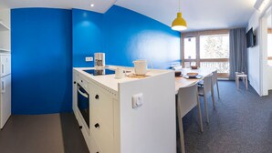 Une cuisine compacte équipée d’une machine à café, d’un réfrigérateur blanc et d’un coin repas avec une table et des chaises.