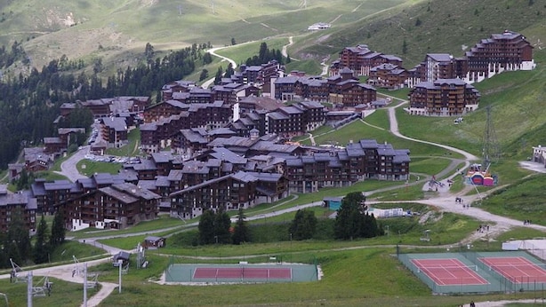 Ein Bergresort mit traditionellen Chaletbauten, kurvenreichen Straßen und einem Tennisplatz.