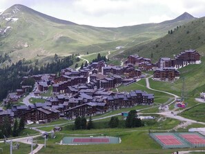 Et bjergresort med traditionelle chalethuse, snoede veje og en tennisbane.