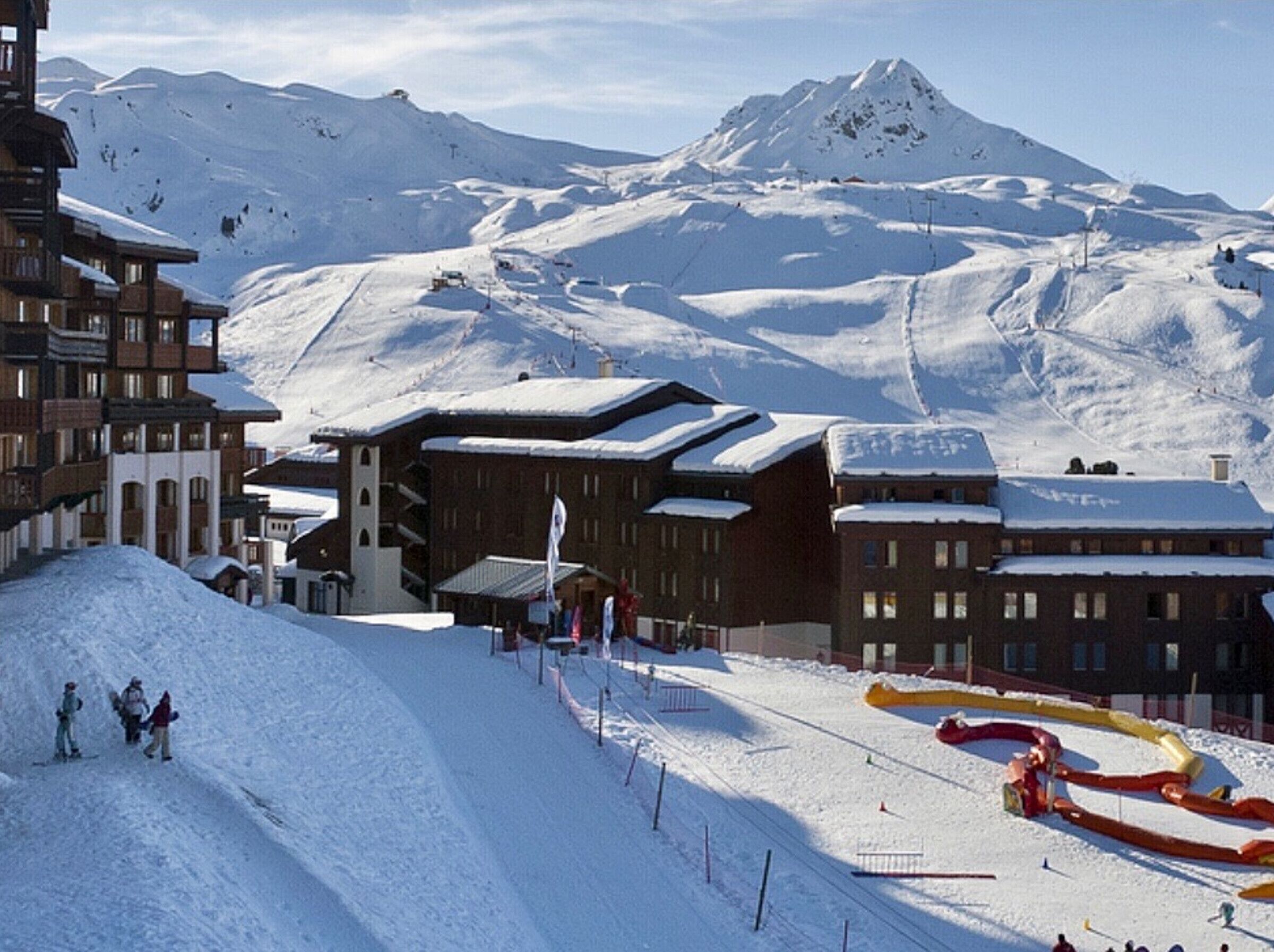 Ein schneebedecktes Skigebiet mit Gebäuden, einer Seilbahn und einem Berg im Hintergrund.