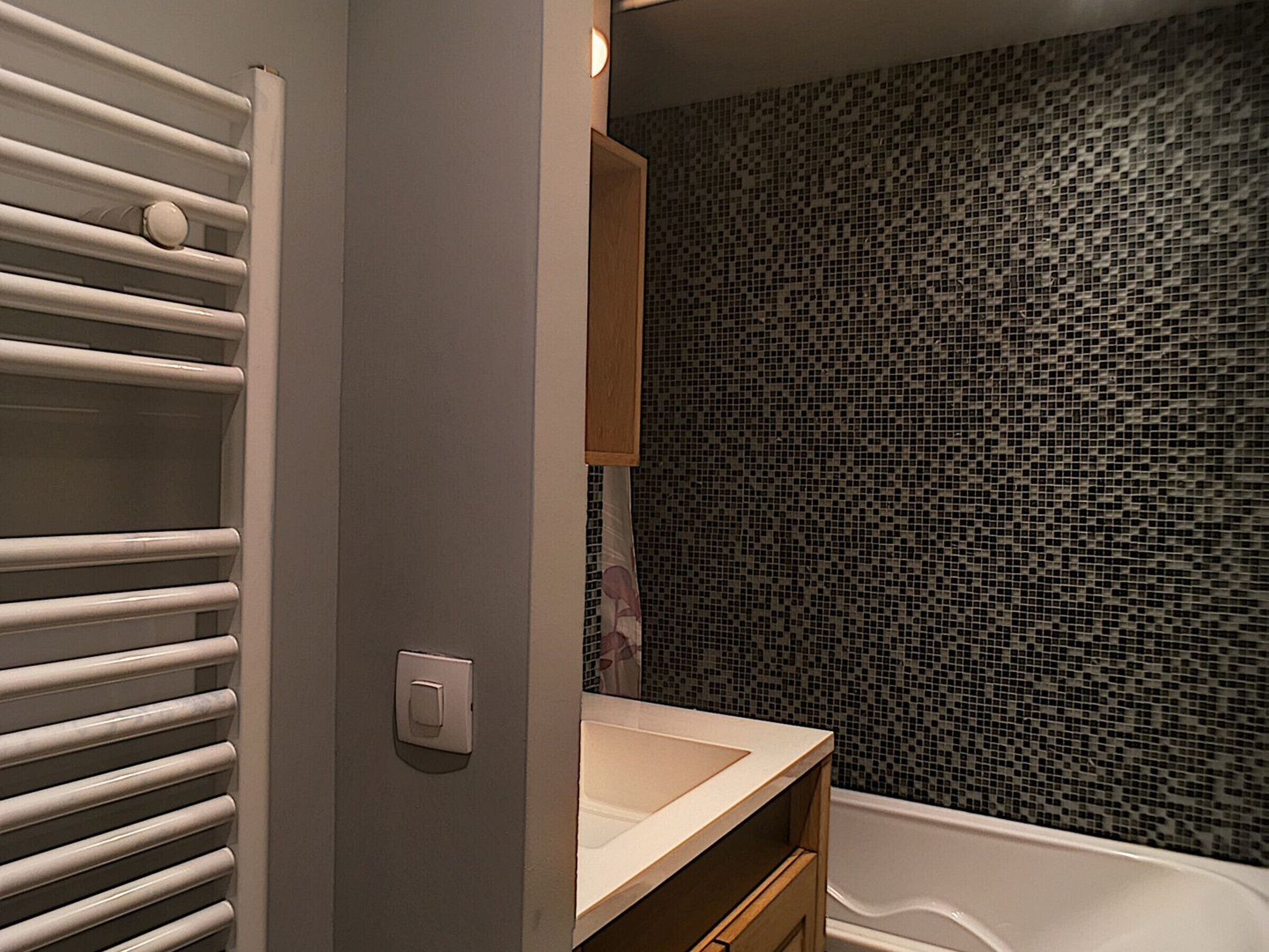 Une salle de bain avec un mur recouvert de carreaux, une baignoire blanche et un porte-serviettes.