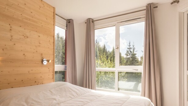 A bedroom with a large bed, wooden panel wall, and a window with curtains. - Spacious 4-room apartment in station center with balcony for 8 people (Les Arcs 1800)