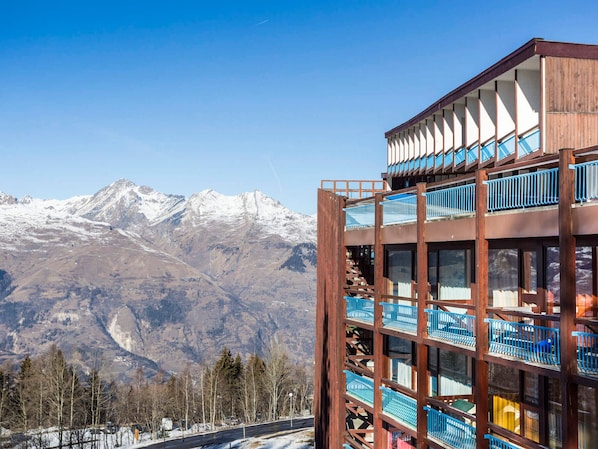 A multi-story building with balconies, set against a mountainous backdrop.