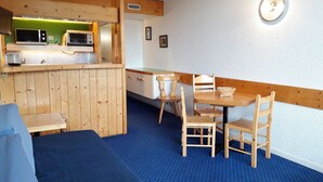 A compact room with a kitchenette, a dining area with wooden furniture, and a blue carpet.