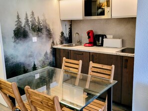 Cozinha moderna com mesa de vidro, cadeiras de madeira e micro-ondas sobre a bancada.