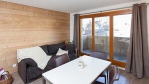 A cozy living area with a wooden wall, a sofa, a dining table, and a sliding glass door leading to an outdoor space.